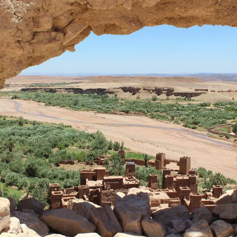 The kasbah of Ait Benhaddou and its palm valley seen from under a rock overhang